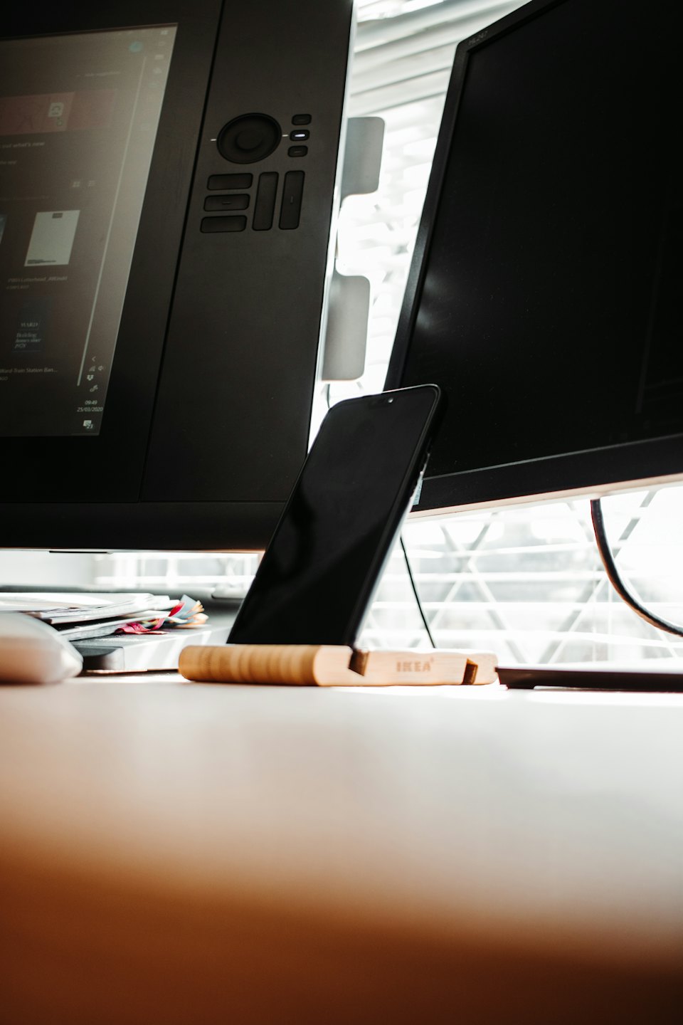 Ein Smartphone steht auf einem Holzständer auf einem Schreibtisch neben Computermonitoren.